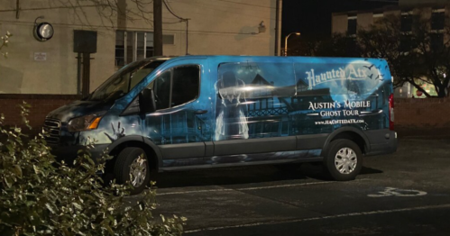 A blue van with a ghostly design, advertising Austin's Mobile Ghost Tour, parked at night.