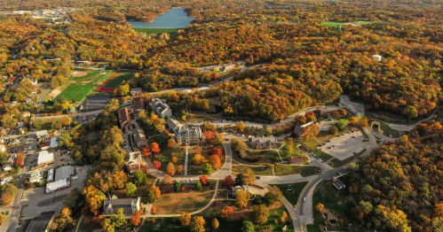 Aerial view of a colorful autumn landscape with trees, a lake, and a small town nestled in the hills.