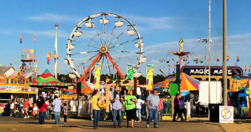 A vibrant carnival scene with a Ferris wheel, colorful rides, and people enjoying the festivities under a clear blue sky.