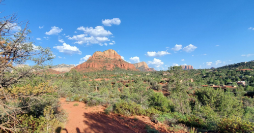 A scenic view of red rock formations and green trees under a blue sky with scattered clouds.