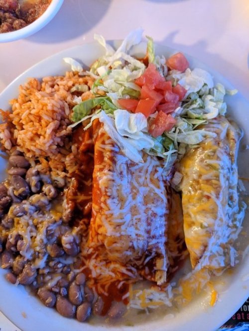 A plate of enchiladas topped with cheese, lettuce, and tomatoes, served with rice and beans on the side.