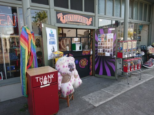 A quirky storefront with colorful decorations, a sign reading "Thank You," and a large furry creature outside.