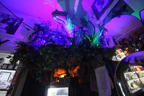 A colorful display featuring a large frog sculpture surrounded by plants and illuminated by purple and green lights.