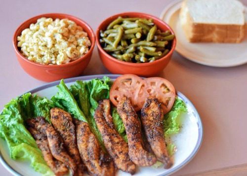 A plate of seasoned fish fillets on lettuce, with bowls of popcorn, green beans, and slices of bread in the background.