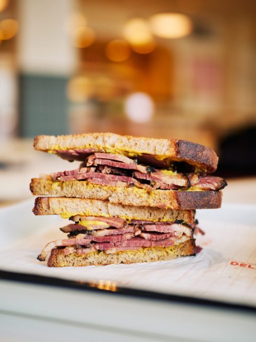 A stacked sandwich with layers of meat, mustard, and pickles, served on toasted bread.