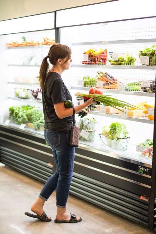 A woman shopping for fresh produce in a grocery store, holding vegetables and browsing the shelves.
