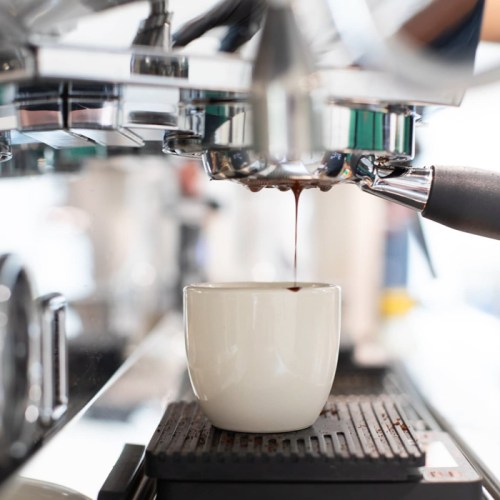 A close-up of espresso being brewed into a white cup from a coffee machine.