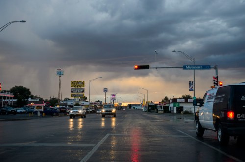 A busy street scene under a cloudy sky, with cars, traffic lights, and various signs in the background.