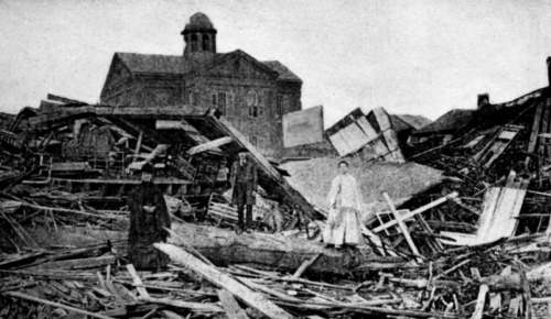 Black and white photo of three people standing amidst rubble and debris from a destroyed building.