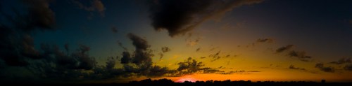 A panoramic view of a sunset with vibrant colors and dramatic clouds against a darkening sky.