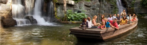 A group of people enjoying a boat ride on a serene river with waterfalls and lush greenery in the background.