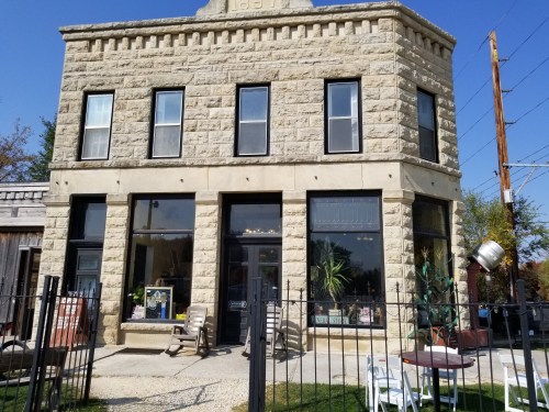 Historic stone building with large windows, a fenced yard, and outdoor seating under a clear blue sky.