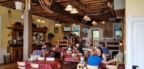 A cozy restaurant interior with wooden beams, tables, and patrons enjoying meals in a warm atmosphere.