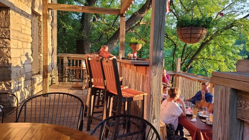 A cozy outdoor dining area with wooden furniture, surrounded by trees and warm evening light.