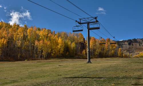 A ski lift stands against a backdrop of vibrant autumn trees and a clear blue sky.