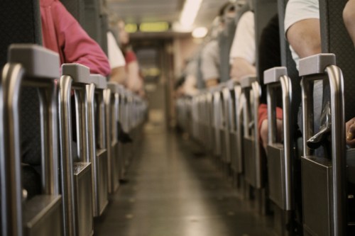 A view down the aisle of a bus, showing rows of seats and passengers' arms resting on armrests.