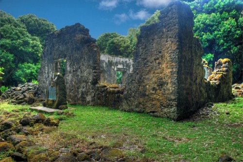 Ruins of a stone structure surrounded by lush greenery and trees under a blue sky.