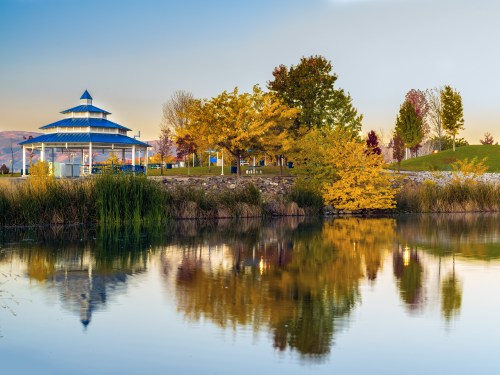 A serene park scene featuring a blue gazebo, colorful autumn trees, and a calm pond reflecting the landscape.