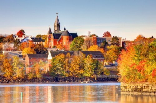 A scenic view of a town with colorful autumn foliage and a church steeple reflected in the water.