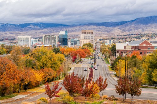 A city skyline surrounded by autumn foliage, with mountains in the background under a cloudy sky.