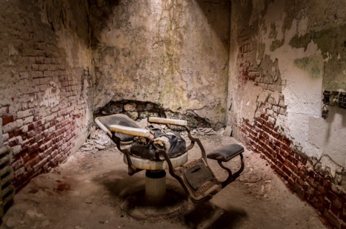 An abandoned, dimly lit room featuring a worn dental chair and peeling walls, evoking a sense of decay and neglect.