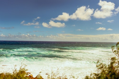 A scenic view of a turbulent ocean under a partly cloudy sky, with waves crashing against the shore.