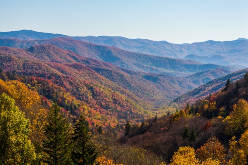 A scenic view of colorful autumn mountains with rolling hills and vibrant foliage under a clear blue sky.