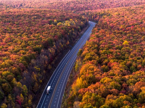 Aerial view of a winding road through vibrant autumn foliage with a truck traveling along the highway.