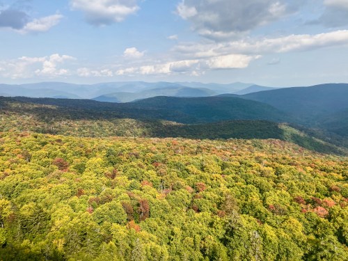 A panoramic view of lush green mountains with hints of autumn colors under a partly cloudy sky.