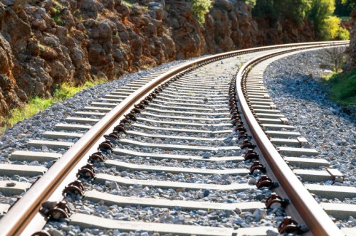Curving railway tracks lined with gravel, surrounded by rocky terrain and greenery.