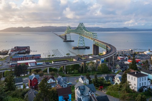 Aerial view of a green bridge spanning a calm bay, with colorful houses and boats in the foreground.