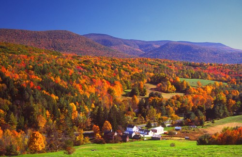 A vibrant autumn landscape with colorful trees, rolling hills, and a small village nestled in the valley.