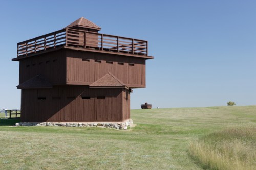 A wooden observation tower on a grassy field under a clear blue sky.