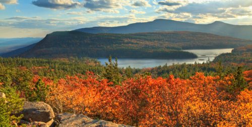 A scenic view of a colorful autumn landscape with mountains, a lake, and vibrant orange and yellow foliage.