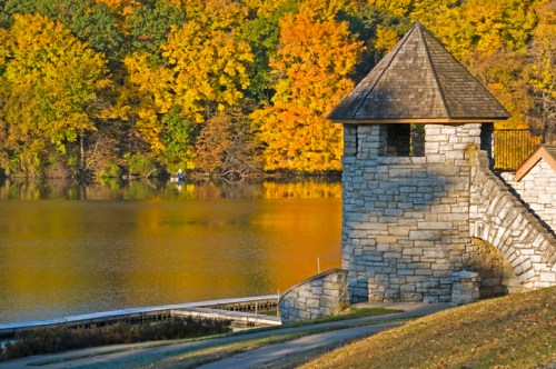 A stone tower by a calm lake surrounded by vibrant autumn foliage.