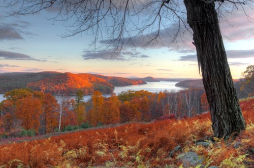 A scenic view of a river surrounded by autumn foliage, with vibrant orange and yellow trees under a colorful sky.