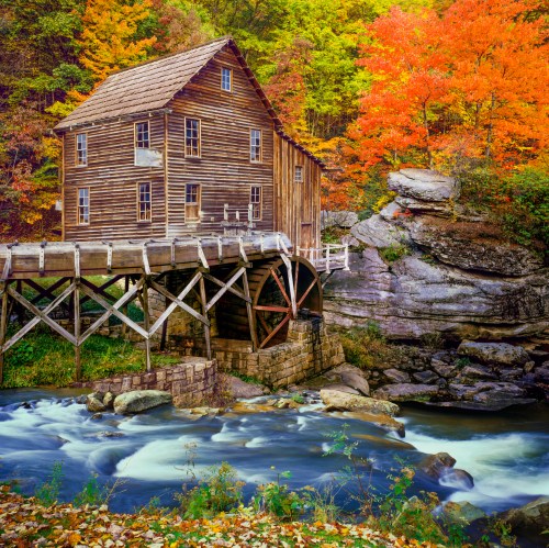 A rustic wooden mill by a flowing river, surrounded by vibrant autumn foliage and rocky terrain.