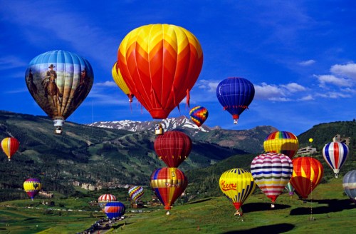A vibrant scene of colorful hot air balloons soaring over a green landscape with mountains in the background.