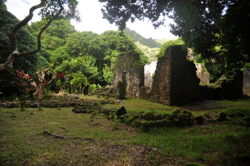 Ruins of an ancient structure surrounded by lush greenery and trees under a bright sky.