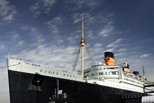The Queen Mary, a historic ocean liner, docked against a blue sky with scattered clouds.