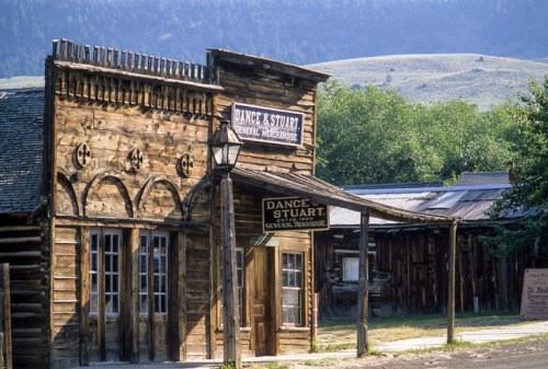 A rustic wooden general store with a sign reading "Dance & Stuart" set against a mountainous backdrop.