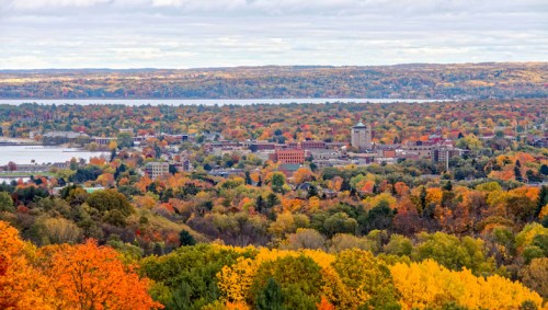 A panoramic view of a colorful autumn landscape with trees in vibrant hues and a small town near a lake.