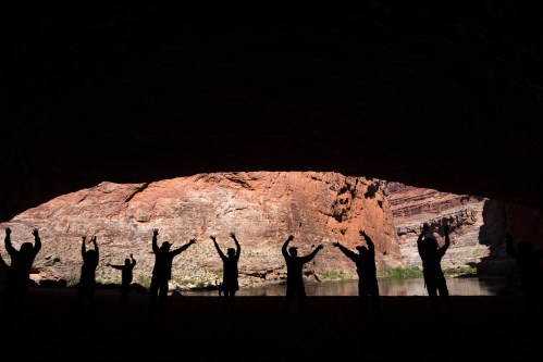 Silhouettes of people with raised arms against a backdrop of a rocky canyon and river.