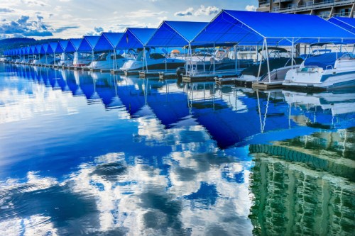 A serene marina with blue-roofed boat slips reflecting in calm water under a cloudy sky.