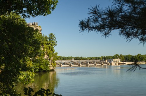 A serene river scene featuring a dam surrounded by lush greenery and clear blue skies.