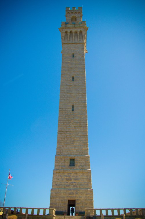 A tall stone tower against a clear blue sky, with a flag visible at the base.