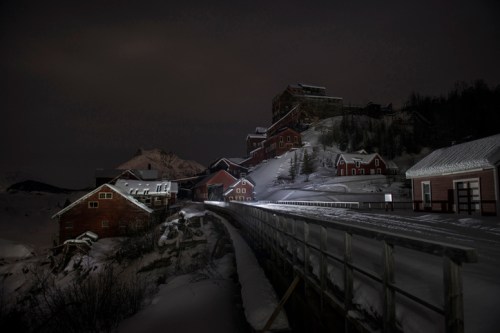 A snowy landscape at night featuring rustic buildings and a winding path, illuminated by soft light.