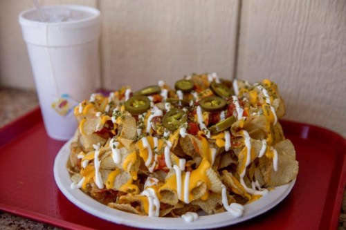 A plate of loaded nachos topped with cheese, jalapeños, and drizzled with sour cream, alongside a drink in a cup.