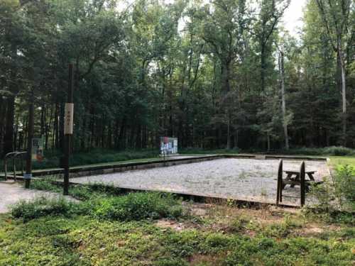 A cleared gravel area surrounded by trees, featuring a picnic table and informational sign in a wooded setting.