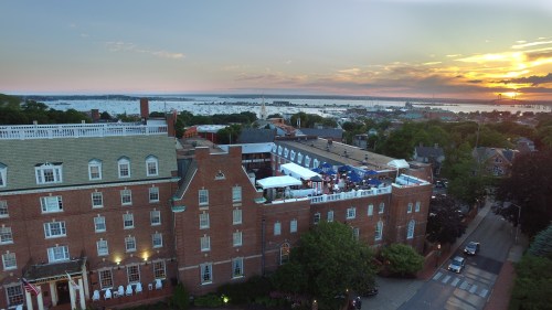 Aerial view of a historic hotel at sunset, overlooking a waterfront and cityscape with lush greenery.